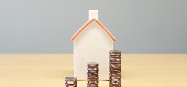 a house and stacks of coins on a table by BuyandRent Homes courtesy of Unsplash.